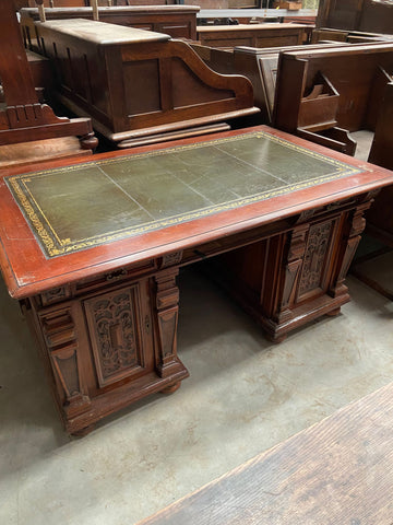 Antique walnut presidential-style office desk with thick ornate carved legs and a green leather top.&nbsp;