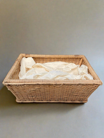 A medium-sized rectangular wicker basket filled with light cream fabric.