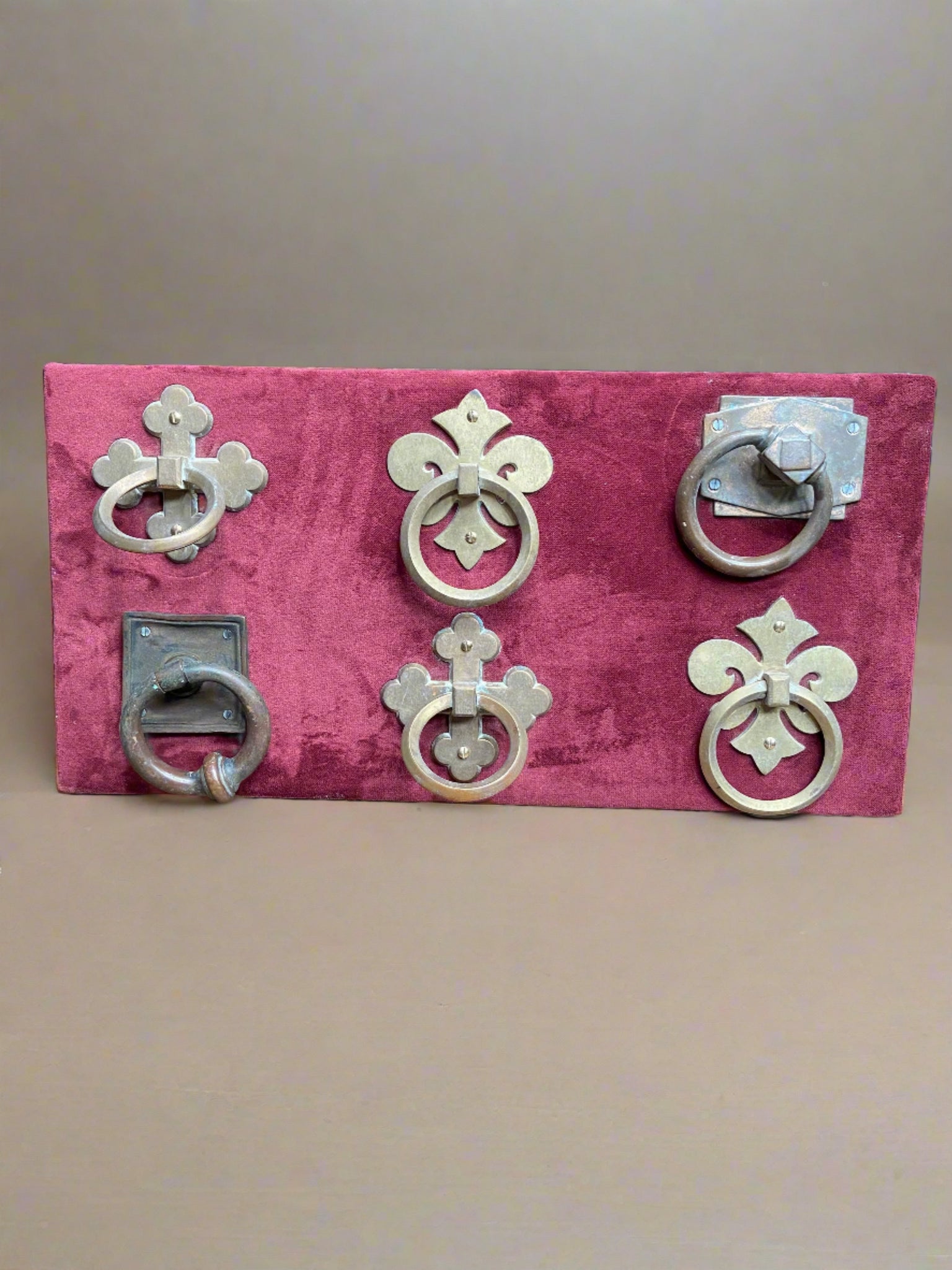 Six solid medieval-style metal knockers mounted on a burgundy fabric board. A useful prop make for cover-ups.