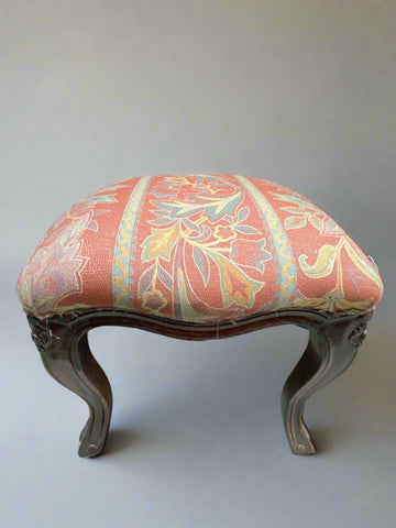 Vintage wooden footstool with cabriole legs, upholstered in a red floral fabric.