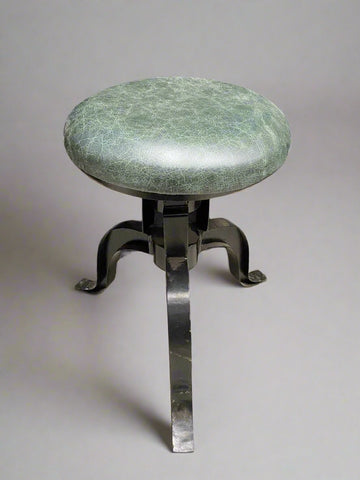 Industrial-style metal piano stool upholstered in mottled green leather fabric.