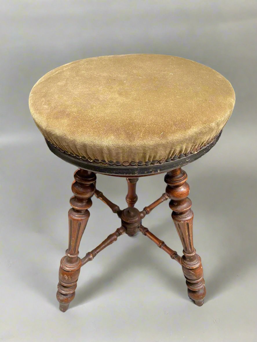 Antique wooden piano stool with turned legs and suede fabric upholstery.