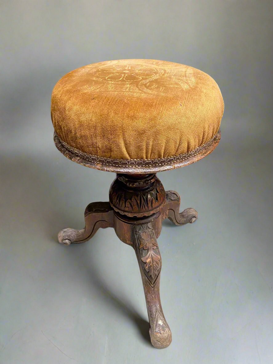 Victorian piano stool with carved oak leaves on the legs and mustard fabric upholstery.