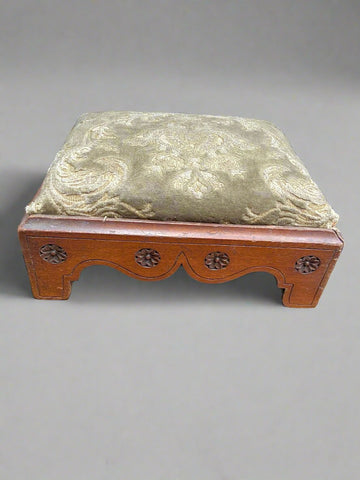 Wooden Victorian footstool with a carved flower design and sage green upholstery.