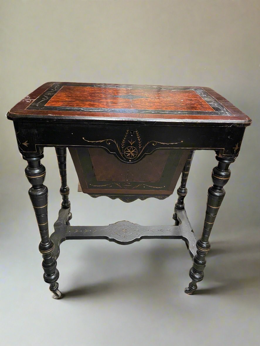 Victorian ebonised wood and amboyna sewing table on wheels with compartment storage.