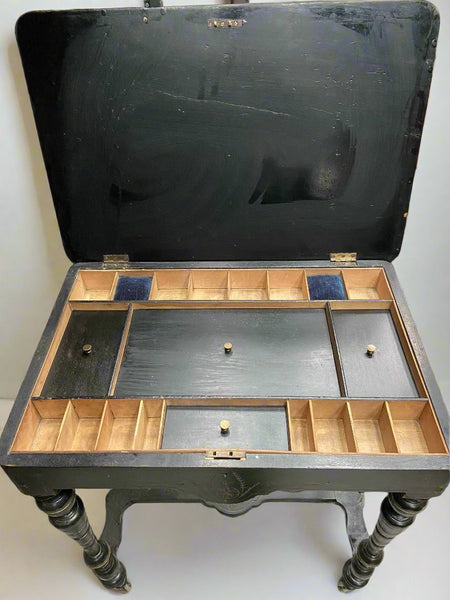 Victorian ebonised wood and amboyna sewing table on wheels with compartment storage.