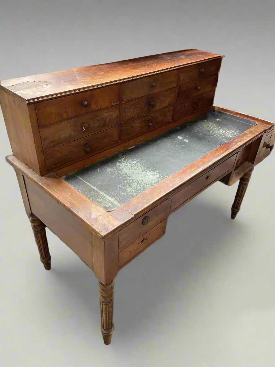 Antique wooden bureau with a green leather top and fourteen drawers.