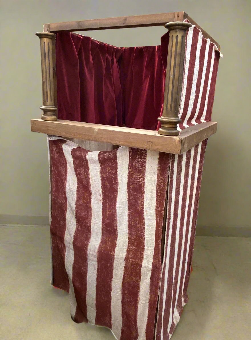 Red and white striped Punch and Judy puppet stall/ theatre, supported by a wooden frame.