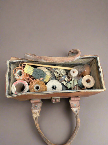 Aged tan leather bag, tied close with a brass buckle. Currently filled with spools of thick thread and wire.