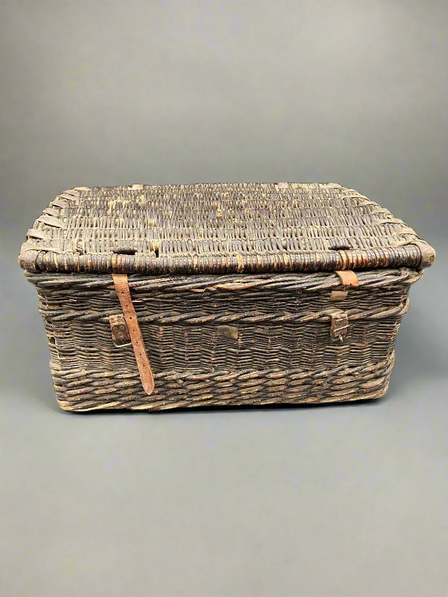 Large worn wicker storage trunk with tan leather straps.