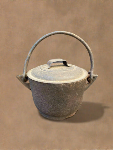 Miniature lidded cast iron cooking pot with a swing handle.