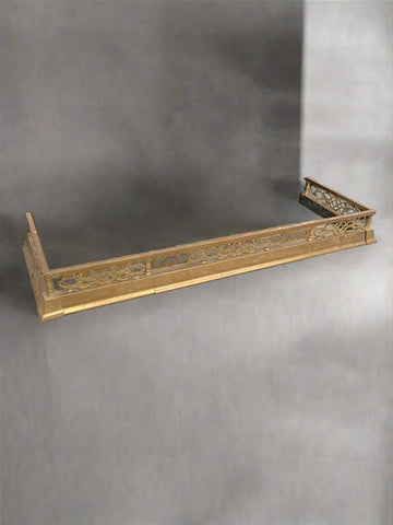 Antique brass fireplace fender with a geometric art deco pattern.