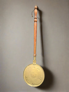 Antique brass bed warming pan with a decorative engraved lid.