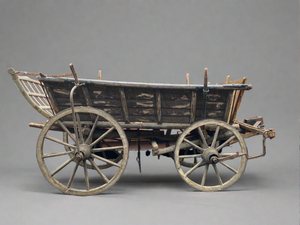 Antique wooden hand cart with a curved, gridded back, suspended by a chain.