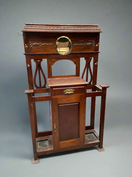 Ornate Edwardian hall stand with a round bevel edged mirror, six coat hooks, detailed brass handles, duo umbrella holders and a storage cabinet.