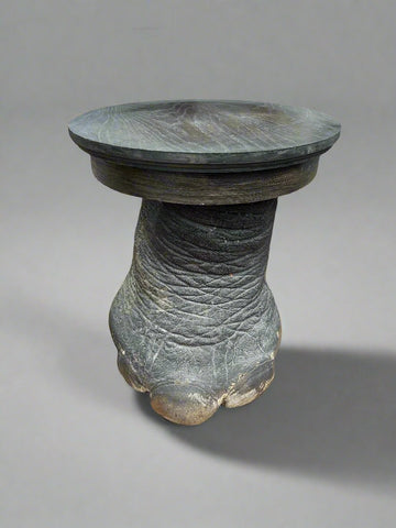 An African black accent table sitting on top of a taxidermy elephant leg.