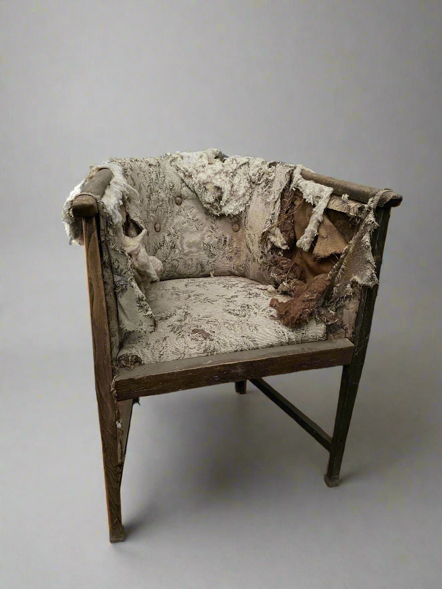 Antique wooden-framed chair with heavily-ripped, cream, floral upholstery.