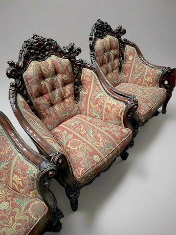 A pair of heavily-carved antique baroque armchairs upholstered in floral red fabric.