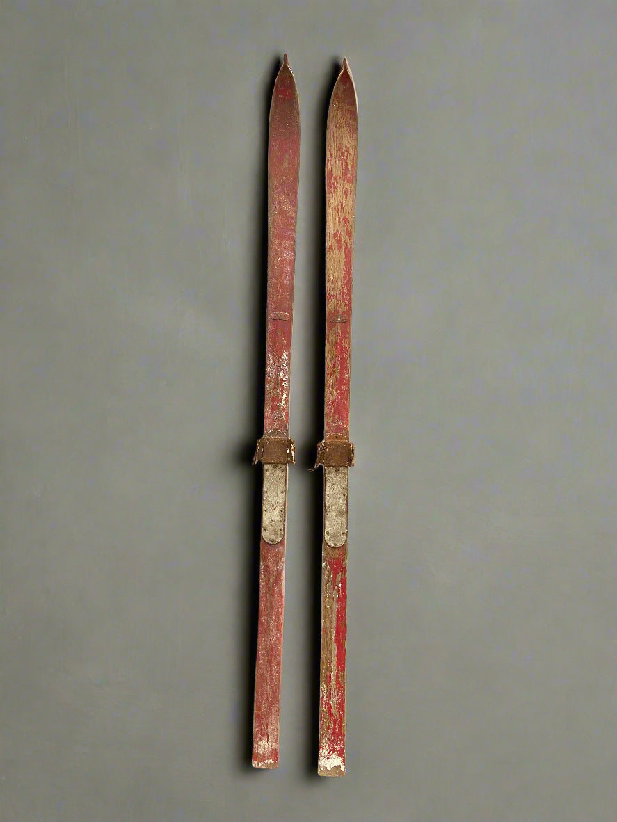 Vintage aged wooden skis with a faded red paint.
