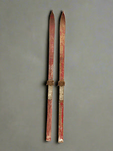 Vintage aged wooden skis with a faded red paint.