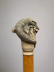 A light wooden walking stick topped with a finely carved ivory handle in the shape of a dolphin.