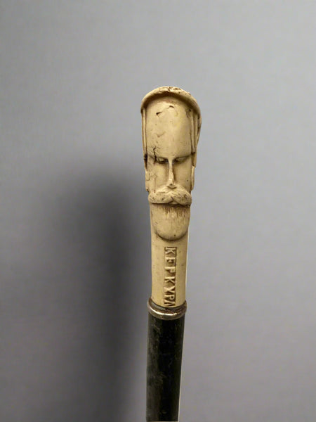 A sleek black gentleman's walking stick topped with a carved ivory handle depicting a male bearded face and a horse head.
