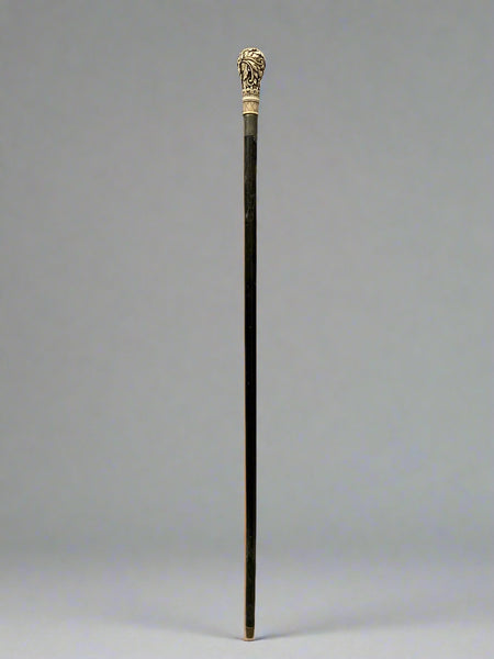 A black ebonised walking stick, topped with a bone handle hand-carved with acanthus patterns.