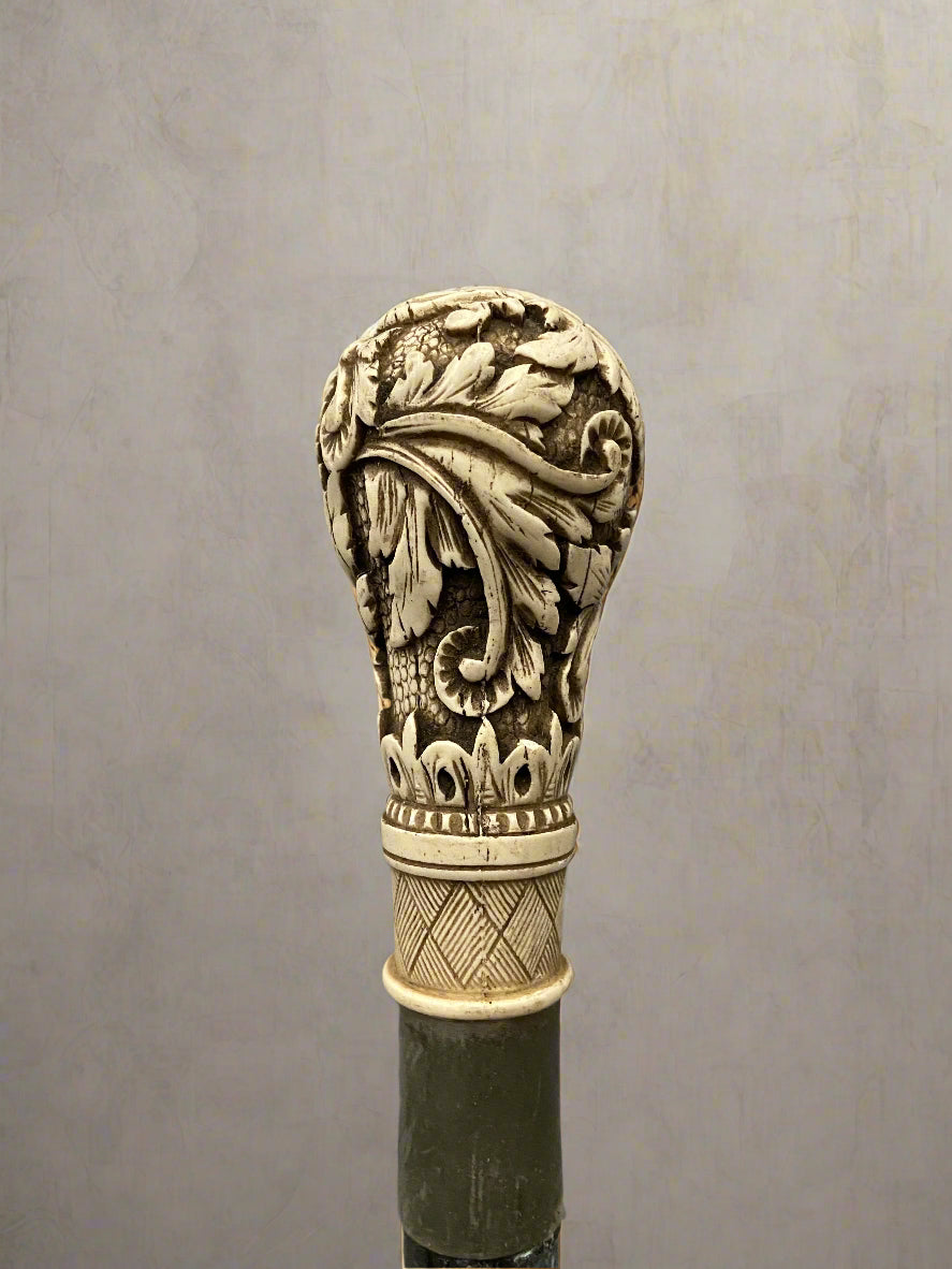 A black ebonised walking stick, topped with a bone handle hand-carved with acanthus patterns.