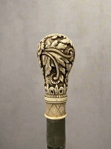 A black ebonised walking stick, topped with a bone handle hand-carved with acanthus patterns.