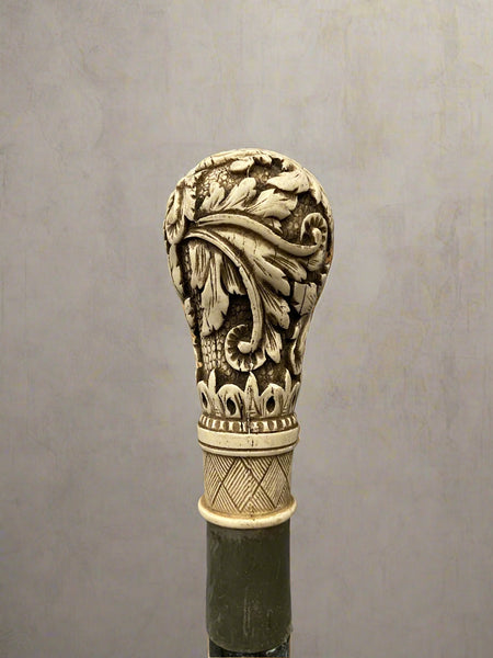 A black ebonised walking stick, topped with a bone handle hand-carved with acanthus patterns.