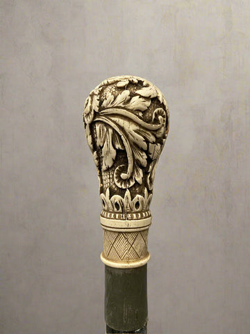 A black ebonised walking stick, topped with a bone handle hand-carved with acanthus patterns.