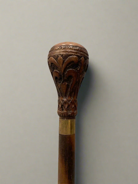 A two-tone wooden walking stick with a carved top and brass strip.