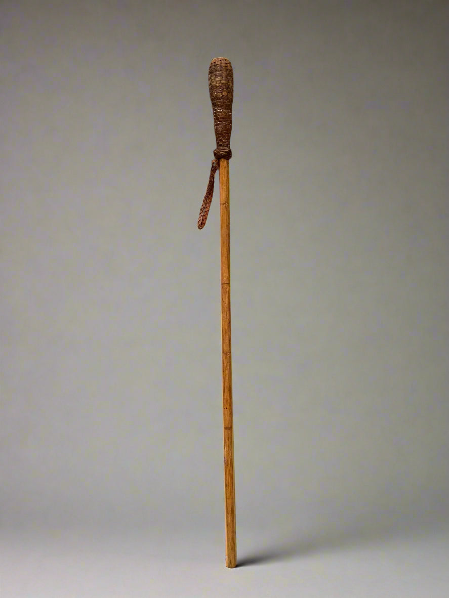 A wooden walking stick with a woven leather handle and strap.