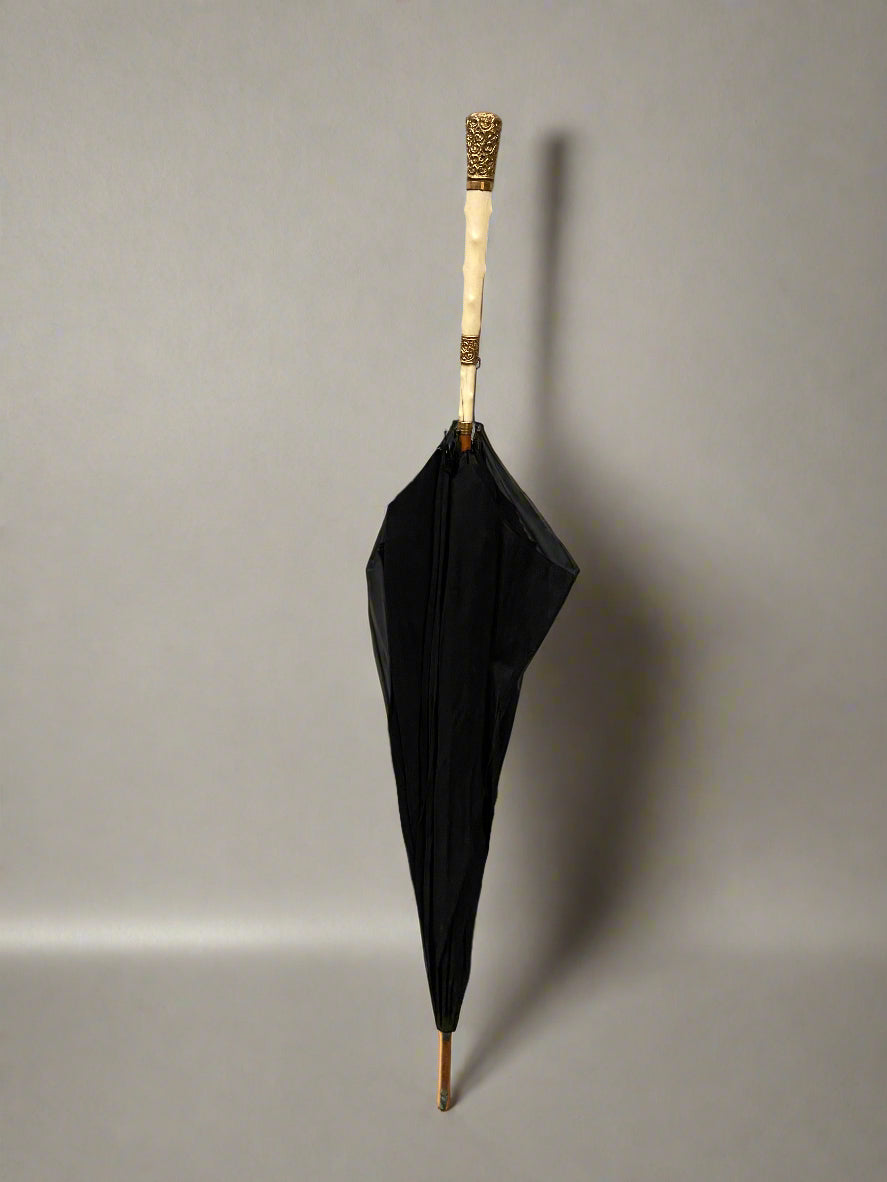 A black parasol with an ivory and gold mounted handle, circa 19th century.