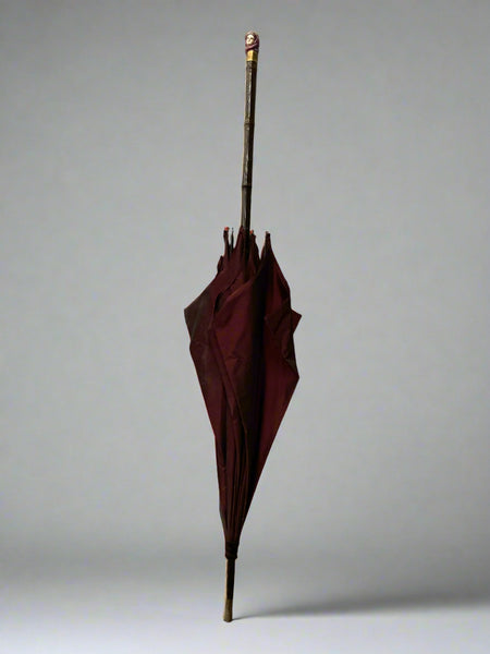 A red fabric umbrella topped with an elegant ceramic lady's head.