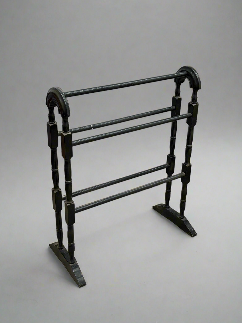 An antique turned black towel rail with a curved frame.