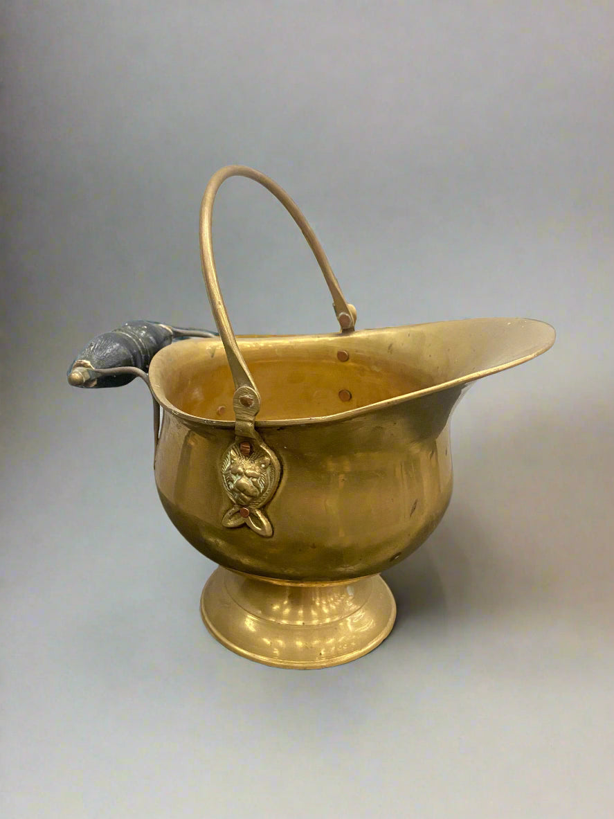 A shiny brass scuttle featuring a wolf face detail and a double handle.