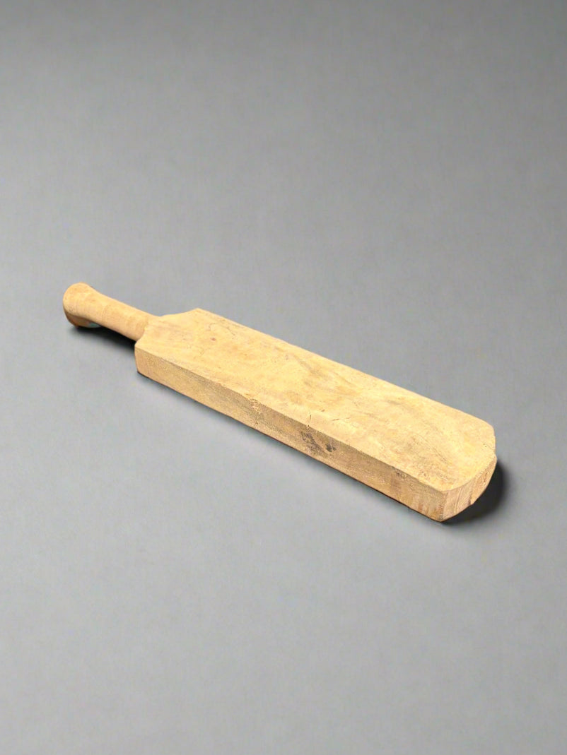 A thick wooden laundry bat/ rug beater, cut from a light coloured wood.