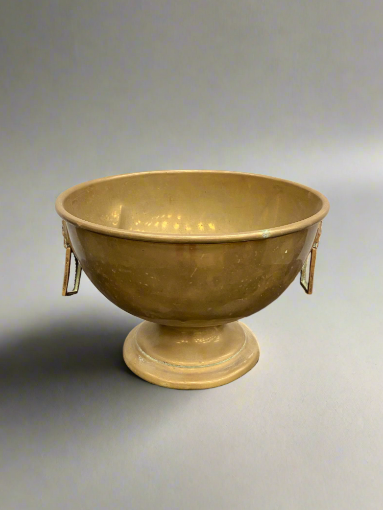 An antique, round, muted brass fruit bowl with square handles.