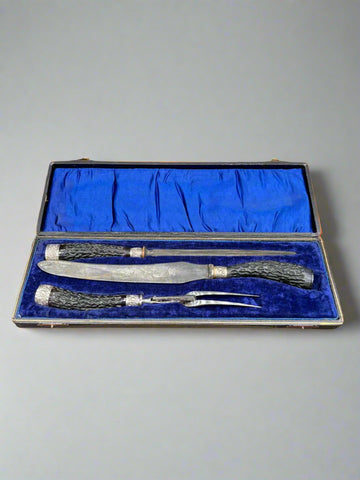 An antique three-piece carving set with antler horn handles. The set comprises of a fork, carving knife and steel inside a blue silk-lined hard case.