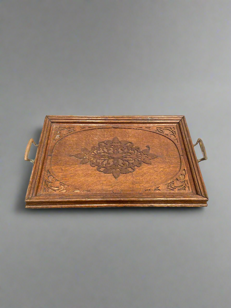 A large wooden serving tray with an intricately carved centre and brass handles.