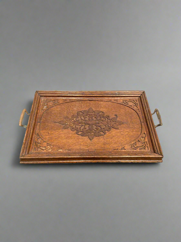 A large wooden serving tray with an intricately carved centre and brass handles.