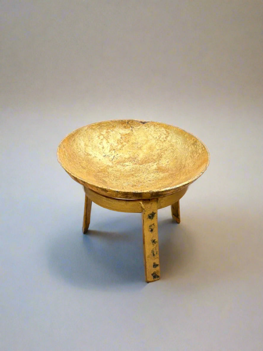 A small antique golden melting bowl with a textured surface, sitting on a tripod stand.
