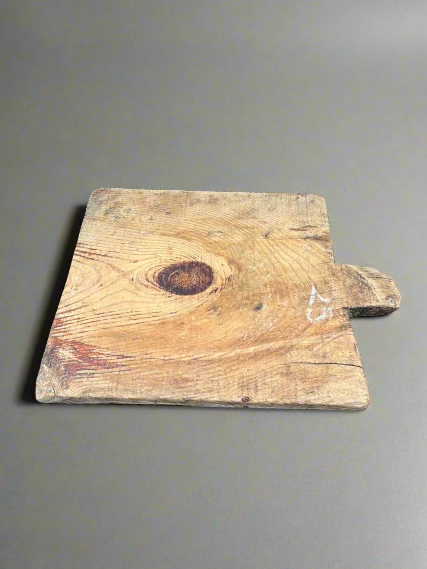 A square-shaped, primitive, wooden bread board.