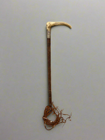 An antique hunting crop with a horn handle wrapped in a silver cuff and leather lash.