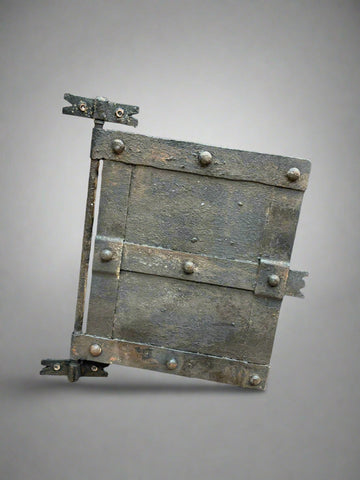 A solid metal medieval window cover with rivets and a textured finish.