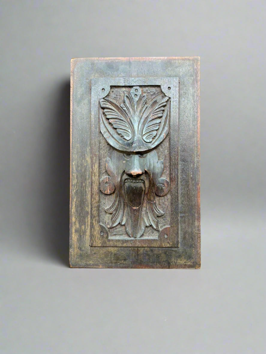A decorative carved wall panel featuring a male howling face with a foliage headdress.