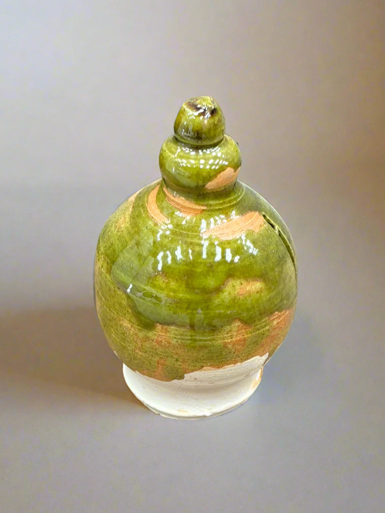 A Tudor-style, round, ceramic money box with a mottled green and orange glaze.