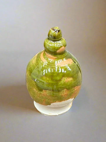 A Tudor-style, round, ceramic money box with a mottled green and orange glaze.