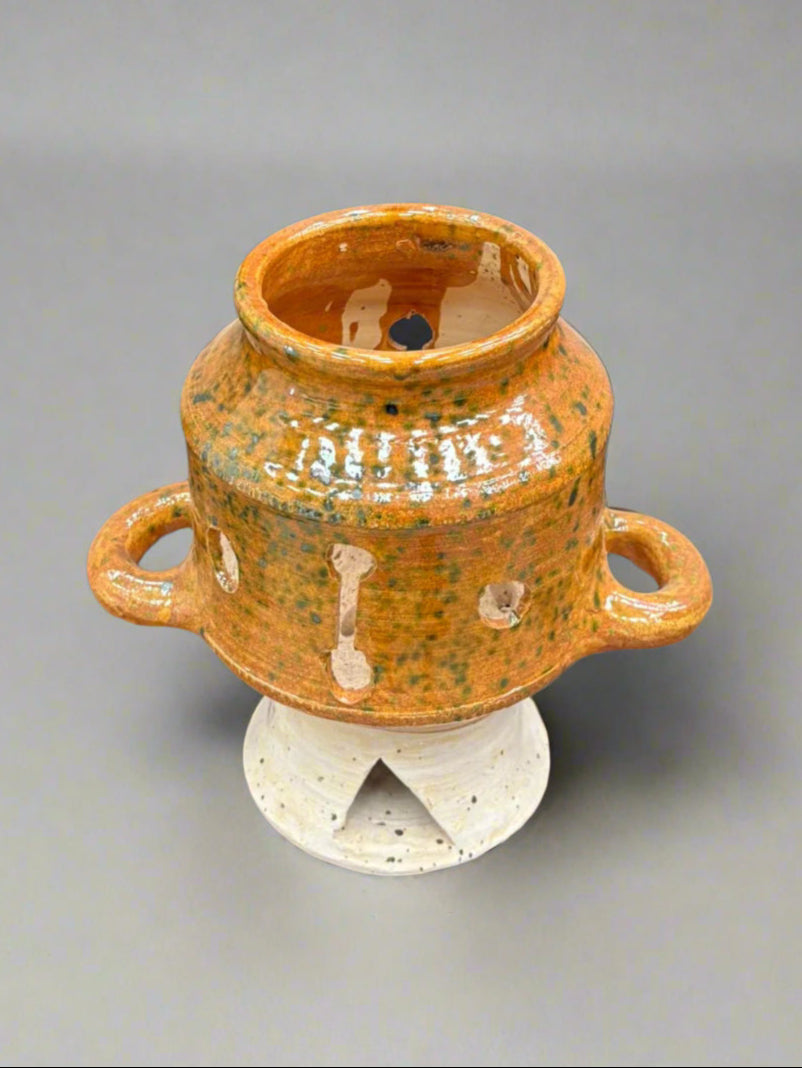 An earthenware ceramic tealight holder with a mottled orange and green glaze and double handles.